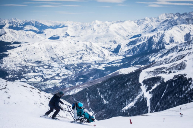 pilote et personne en fauteuil ski sur une piste, belle vue sur une vallée
